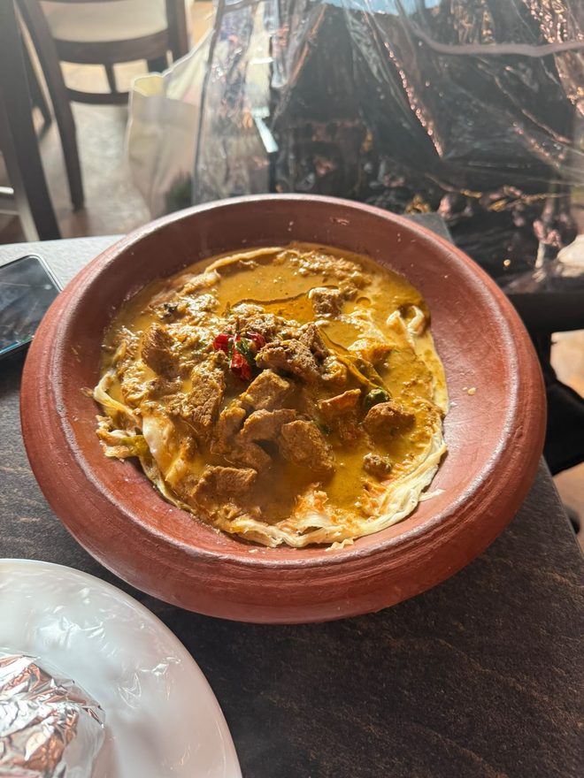 A meat curry in a terracotta clay pot on a marble table