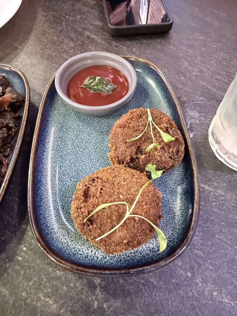Two fried cutlets on an oval blue plate with a pot of red dipping sauce