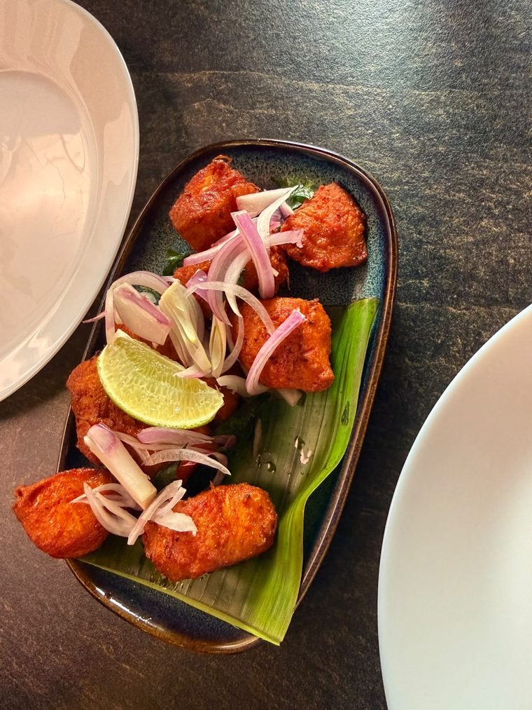 Red-spiced fried chicken pieces with lime and sliced onion on a banana leaf