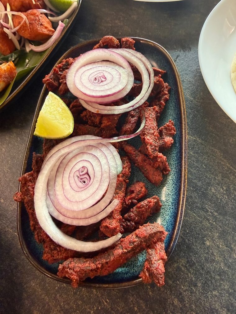 Dry-fried spiced beef strips with onion rings and lime on a dark oval plate
